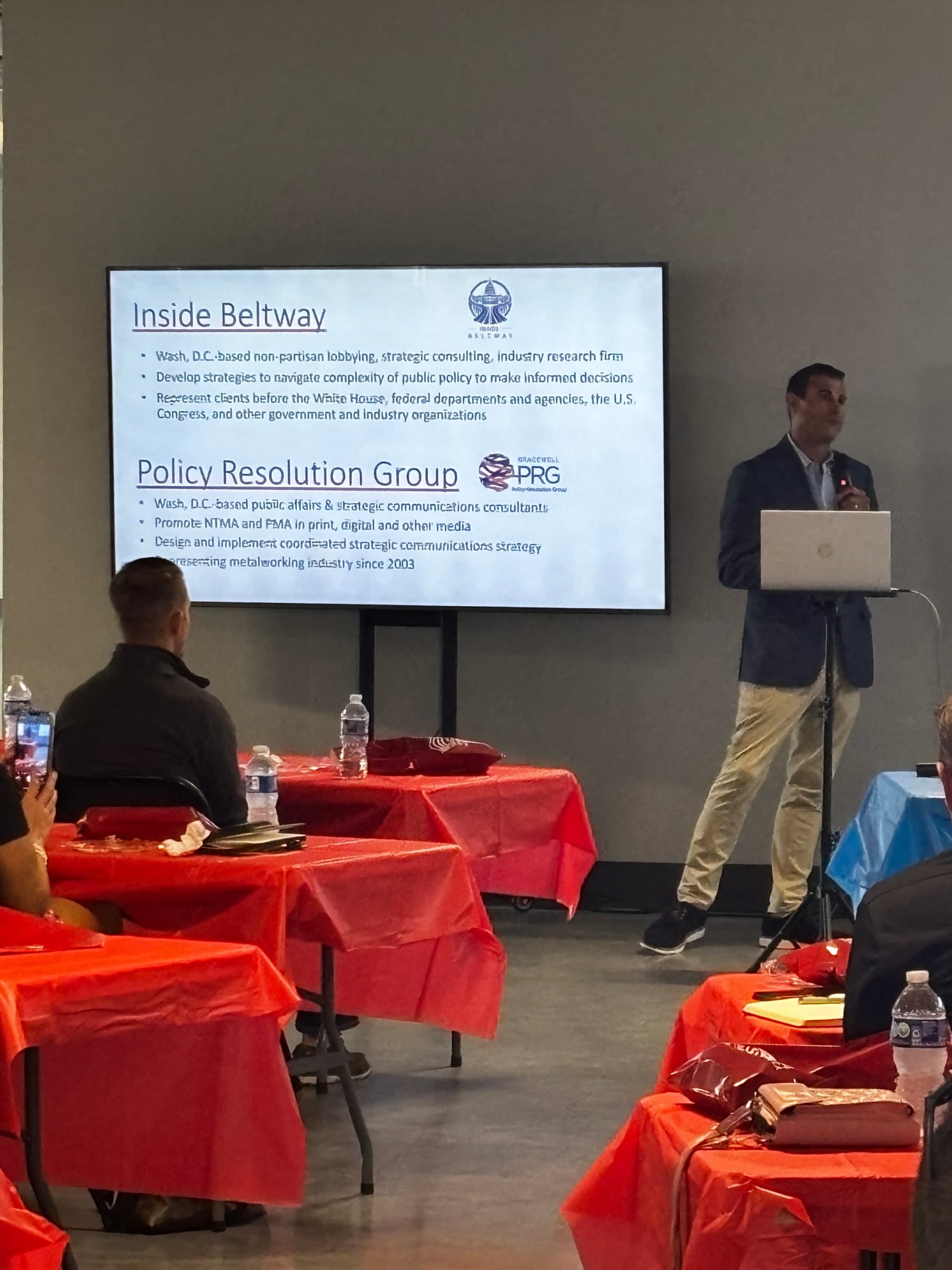 A presenter at a laptop beside a slide introducing Inside Beltway and the Policy Resolution Group