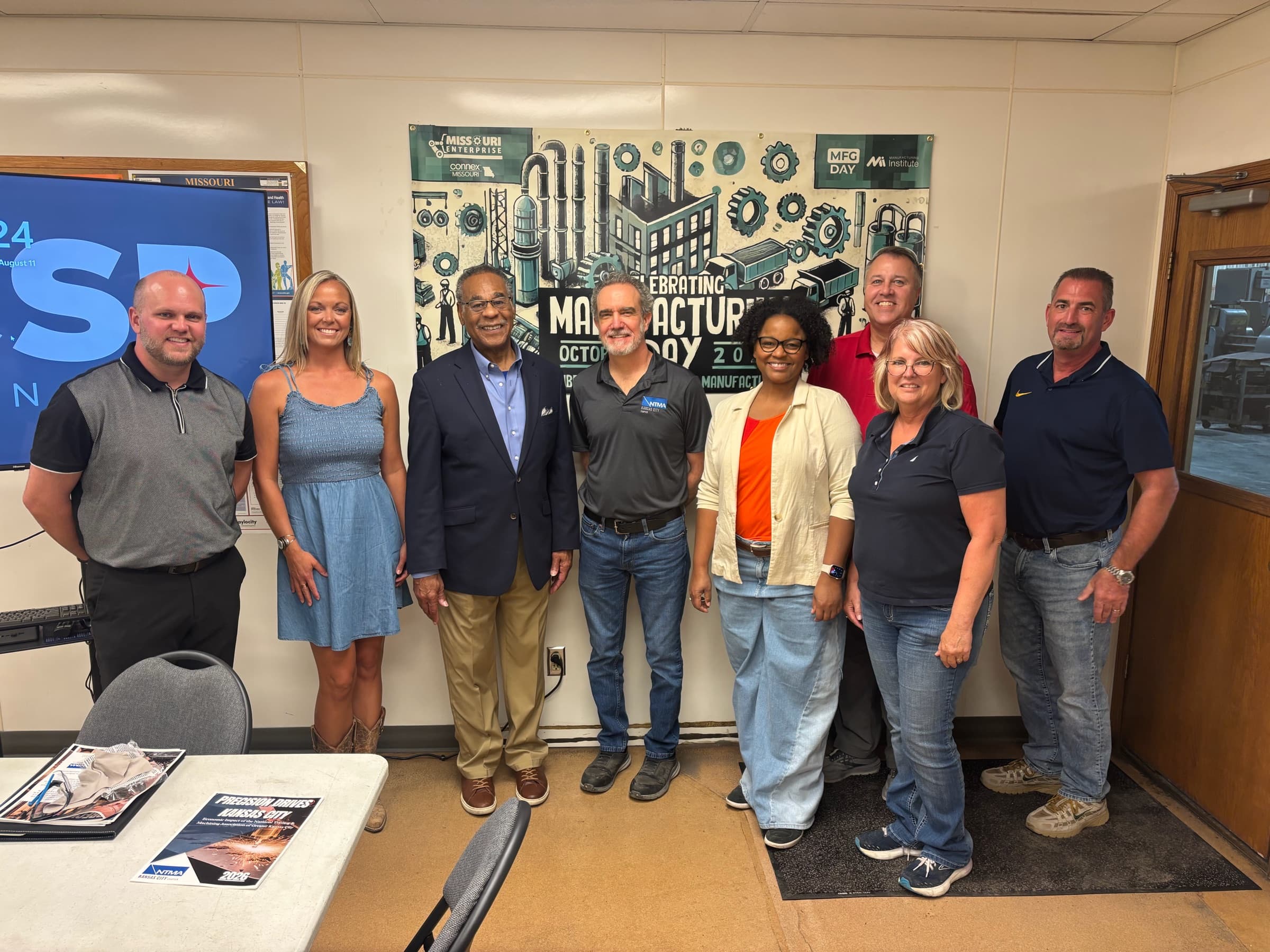 Congressman Emanuel Cleaver with seven members in front of a Manufacturing Day poster