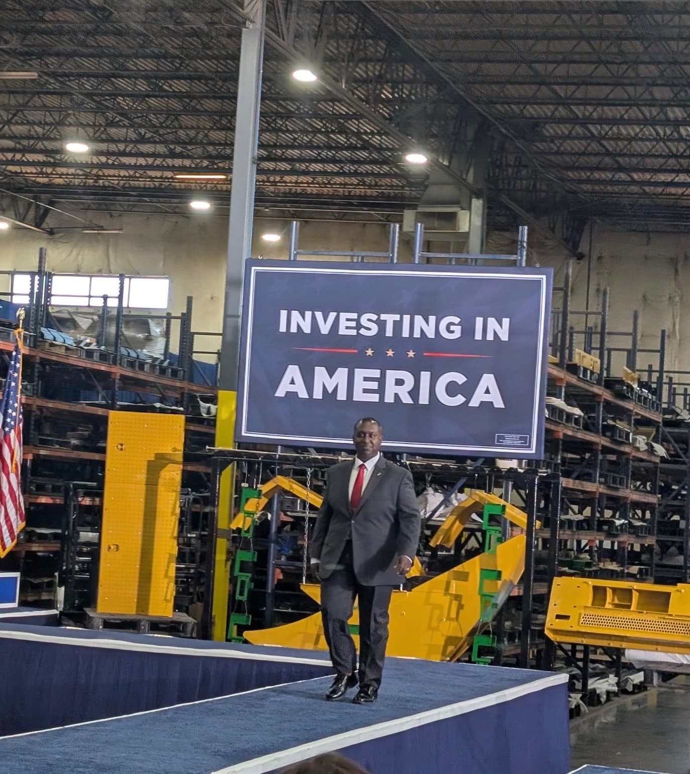 A speaker walking to the podium beneath an Investing in America sign on a plant floor