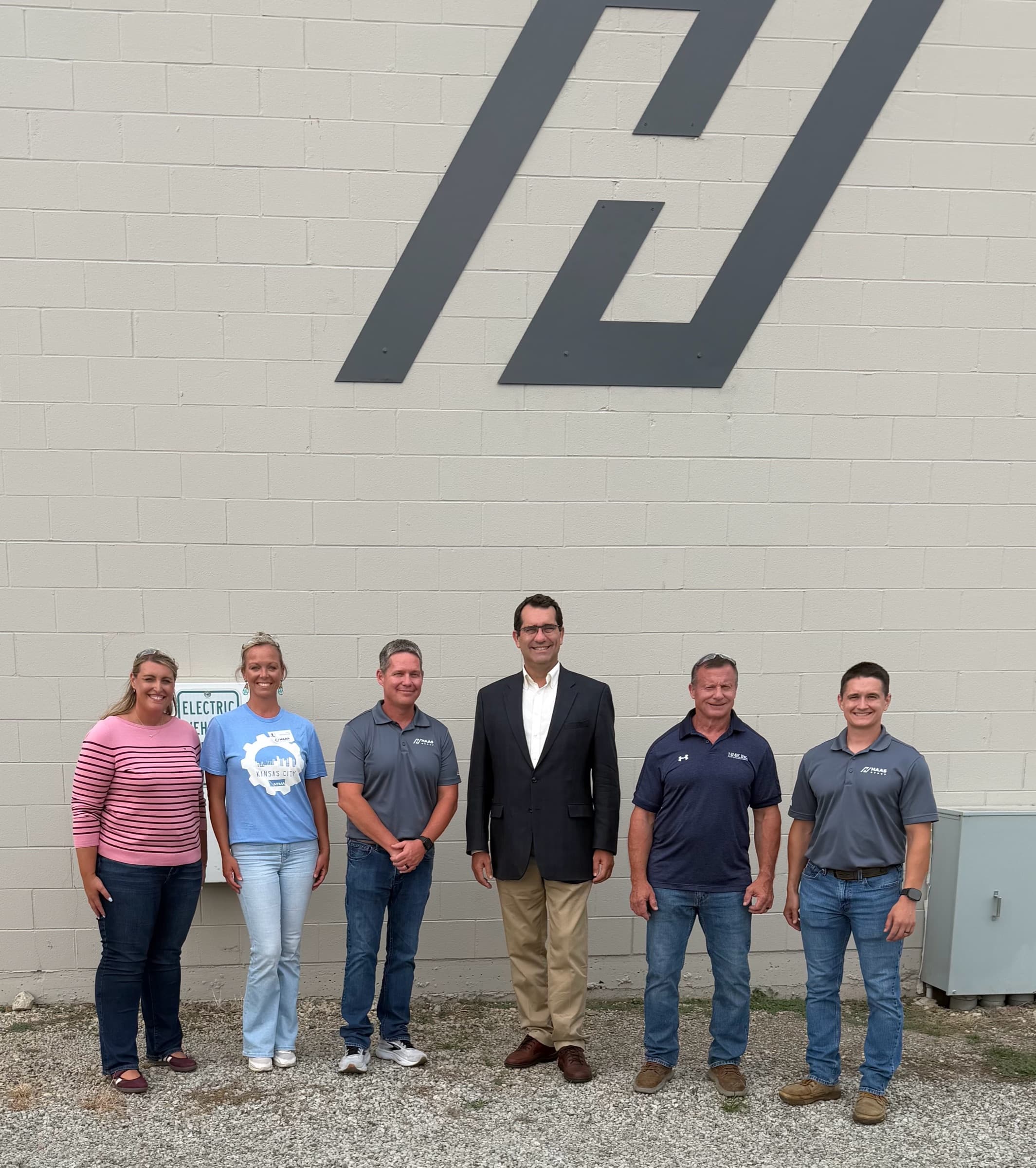 Congressman Derek Schmidt with five members outside a plant beneath a large HME logo