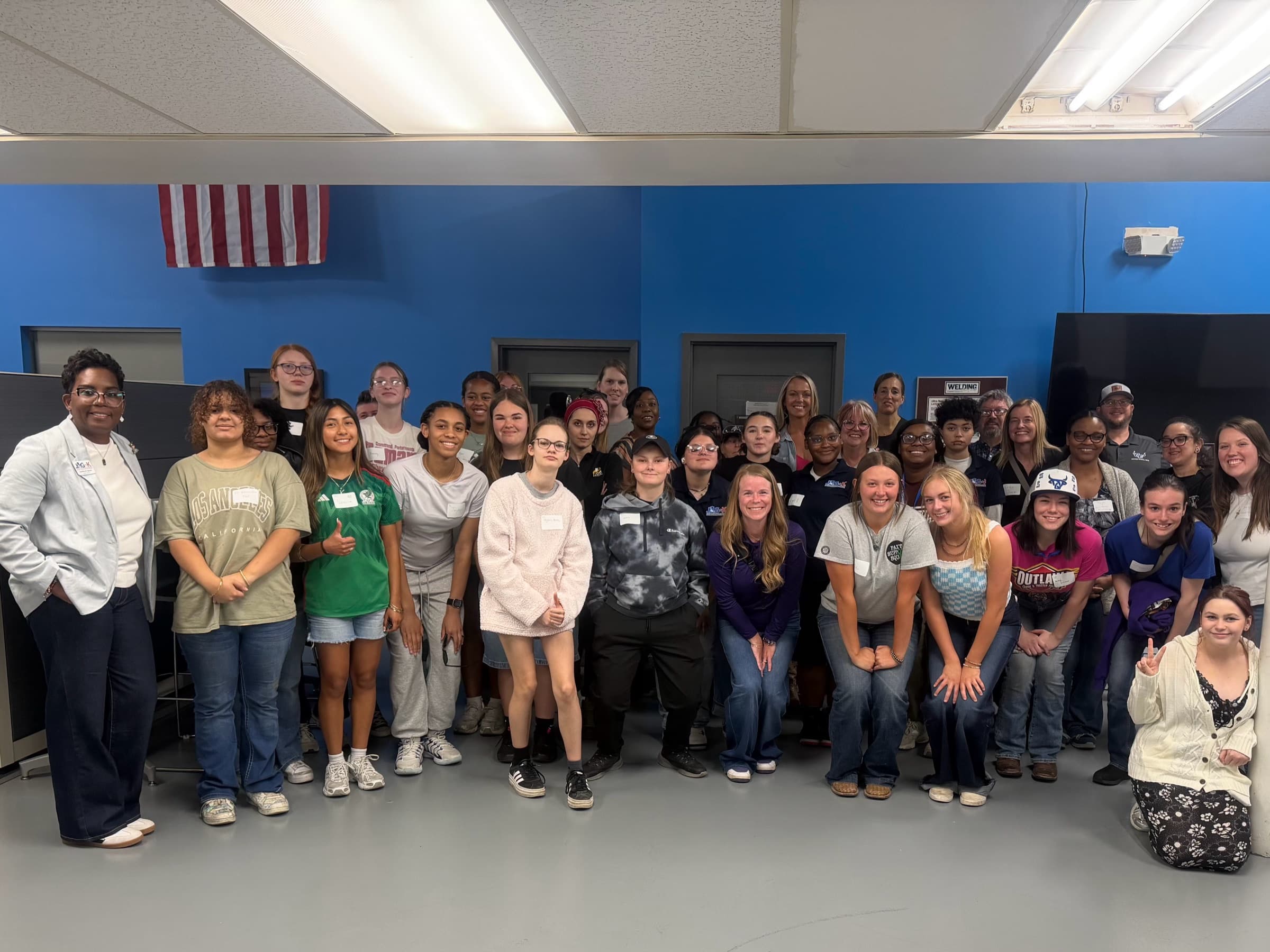 Around thirty high school students and their hosts standing together in a classroom under an American flag
