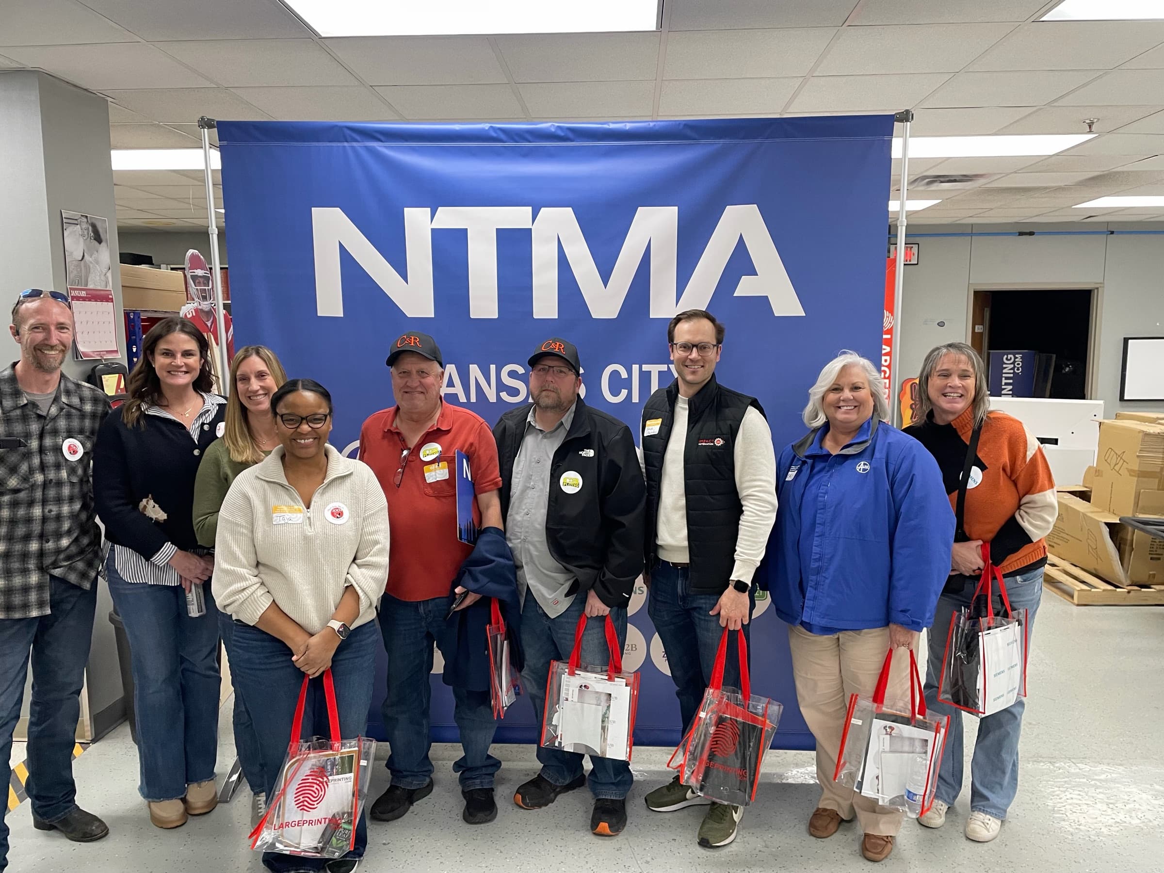 Ten chapter members with tote bags in front of a Kansas City NTMA banner