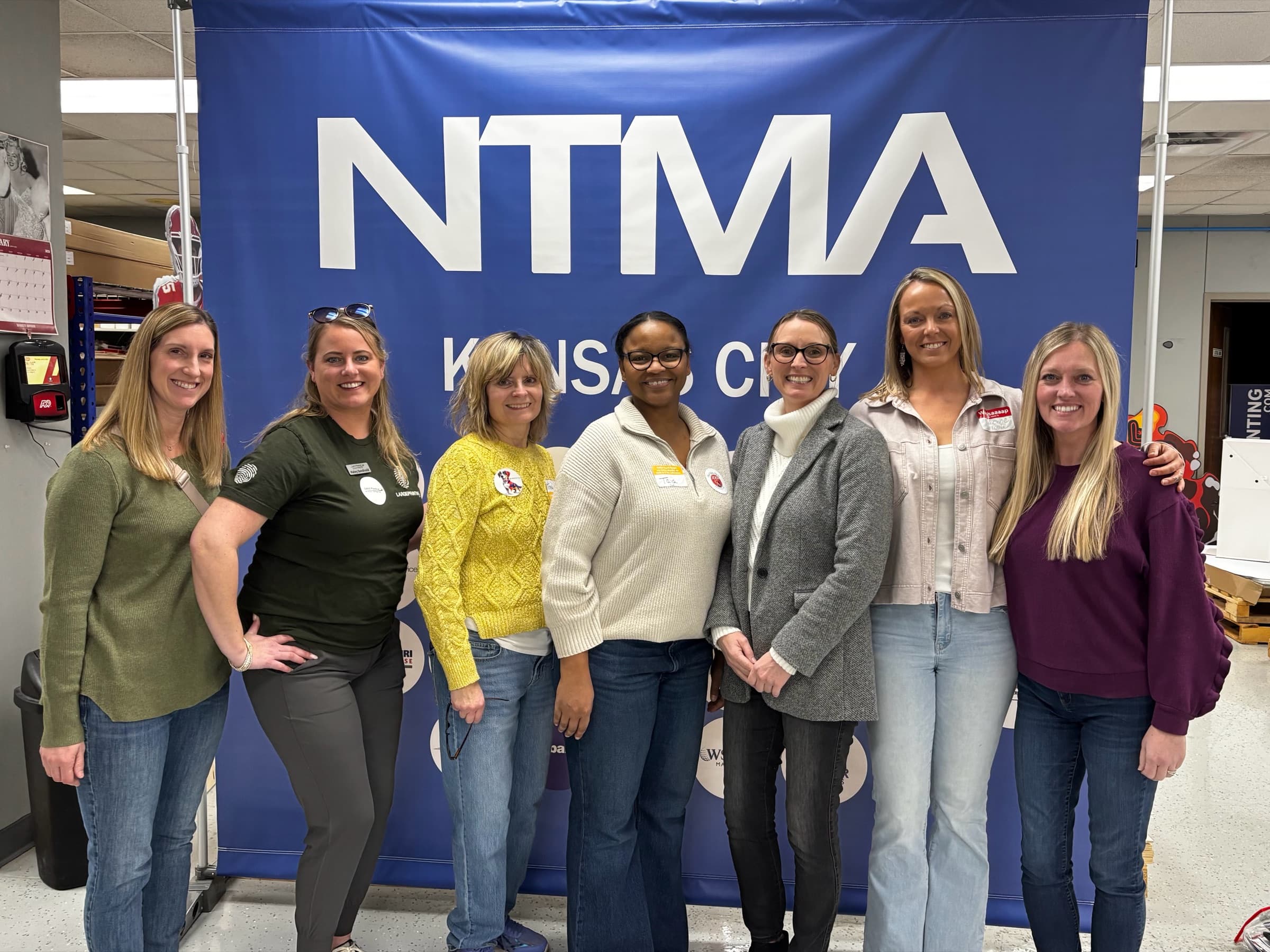 Seven women standing together in front of a Kansas City NTMA banner