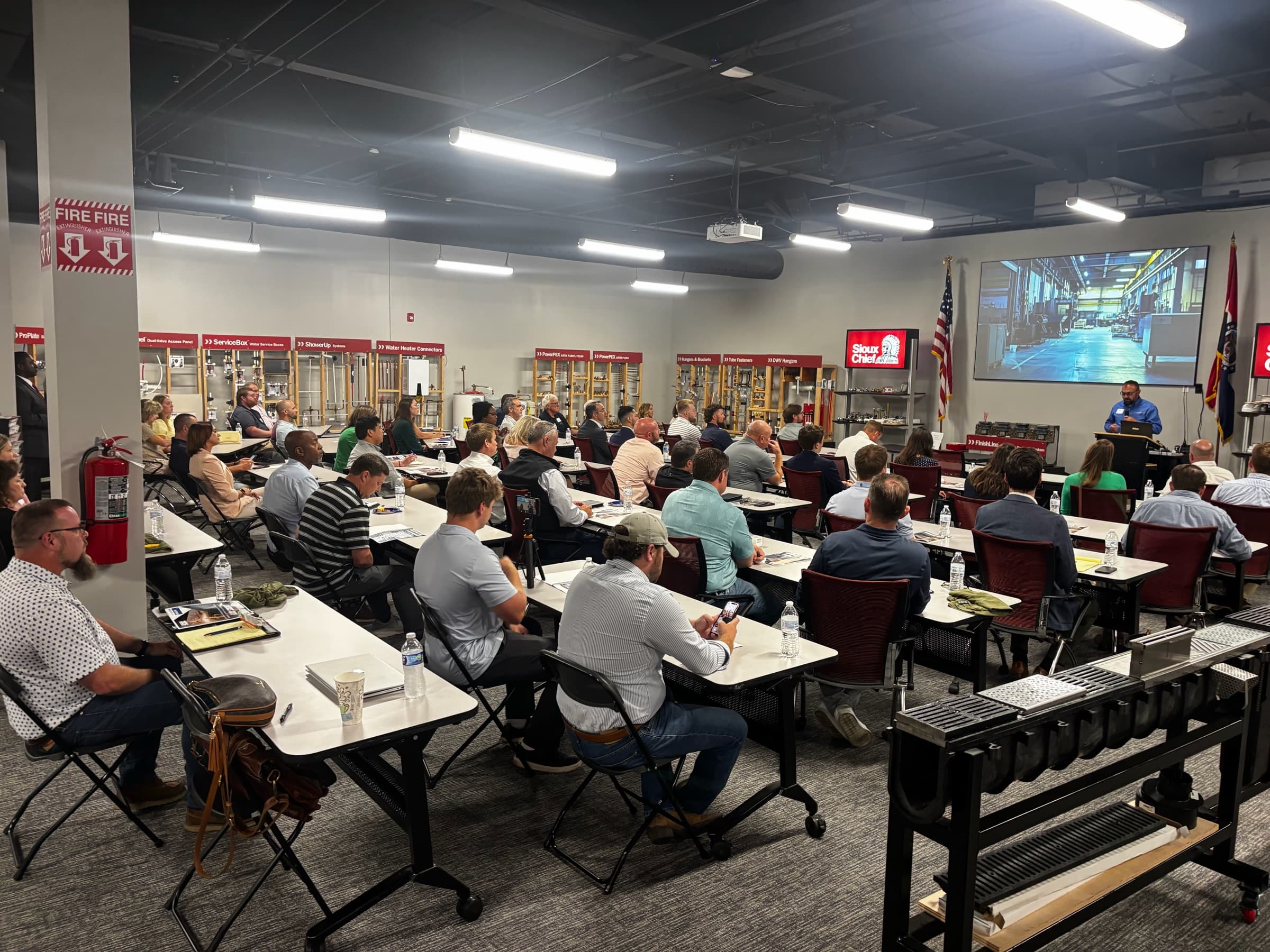 A full room of members at tables watching a presentation on a screen inside a member training room