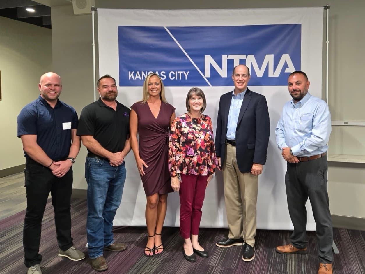 Six people, including the Kansas State Treasurer, in front of a Kansas City NTMA banner at the Precision Drives Kansas City launch