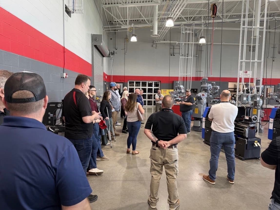 A group of adults watching an instructor at a milling machine in a red-and-grey training lab