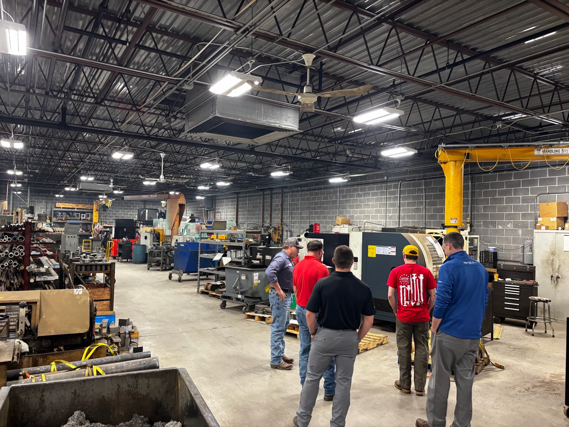 Four members looking over a CNC lathe on a shop floor during a tour