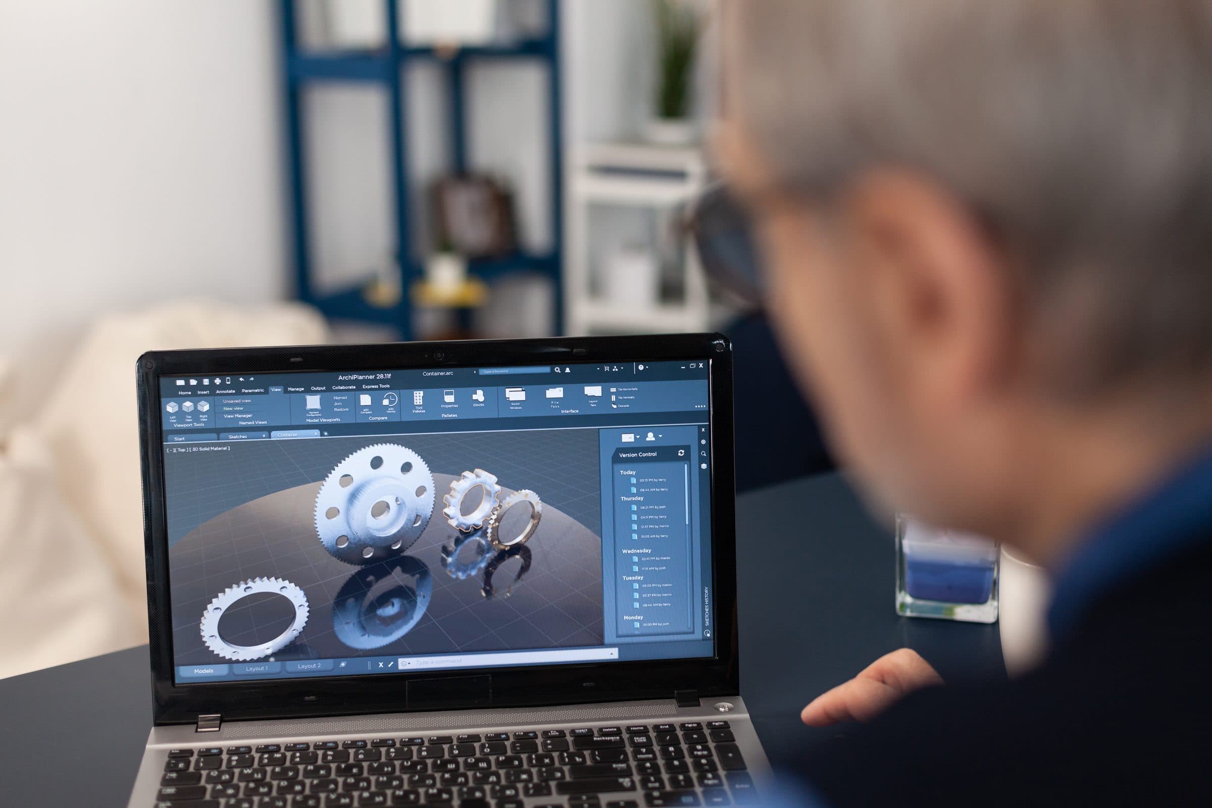 A man reviewing a 3D gear model on a laptop in a workshop