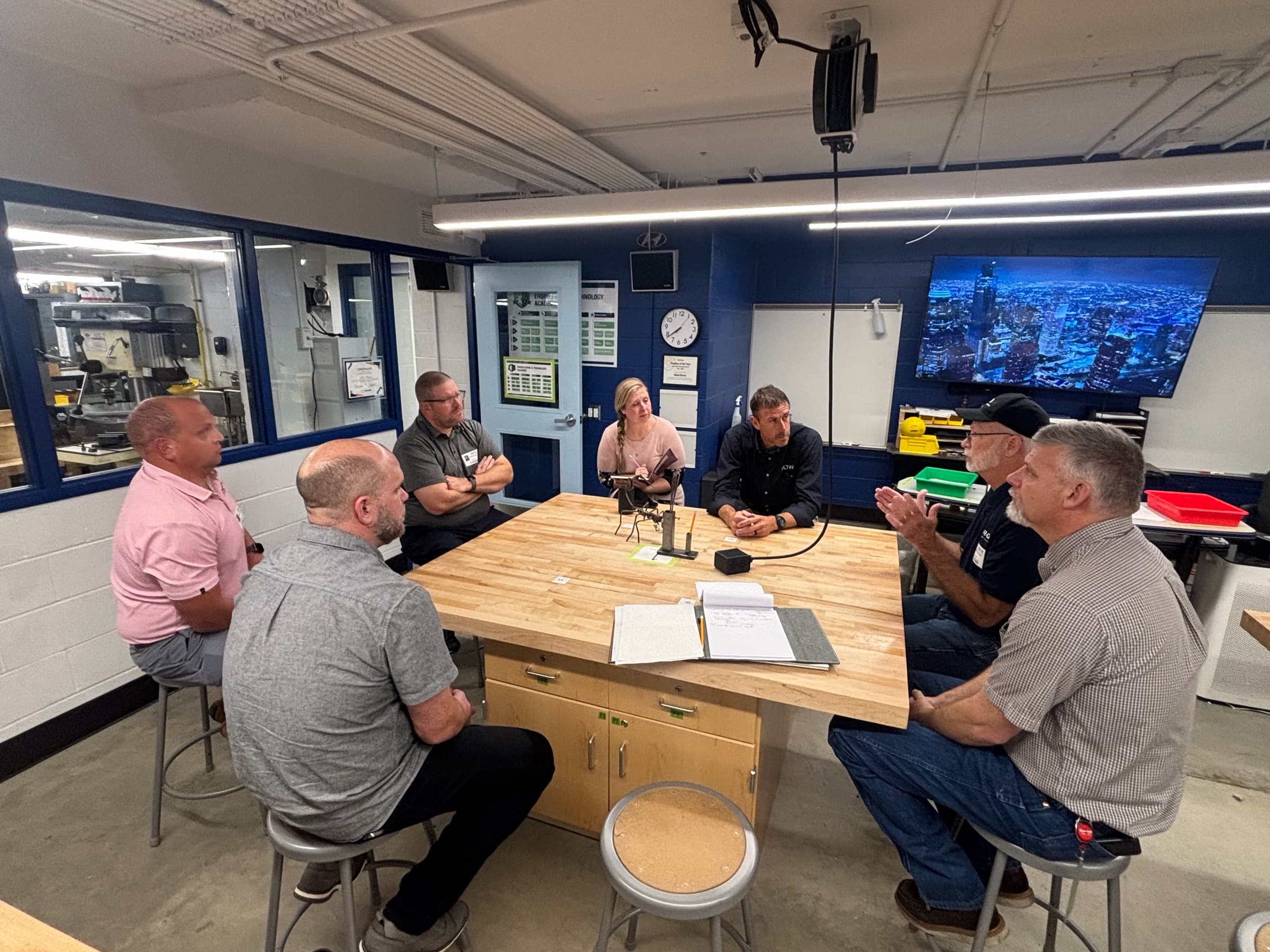 Six people in discussion around a workbench in a school machine shop