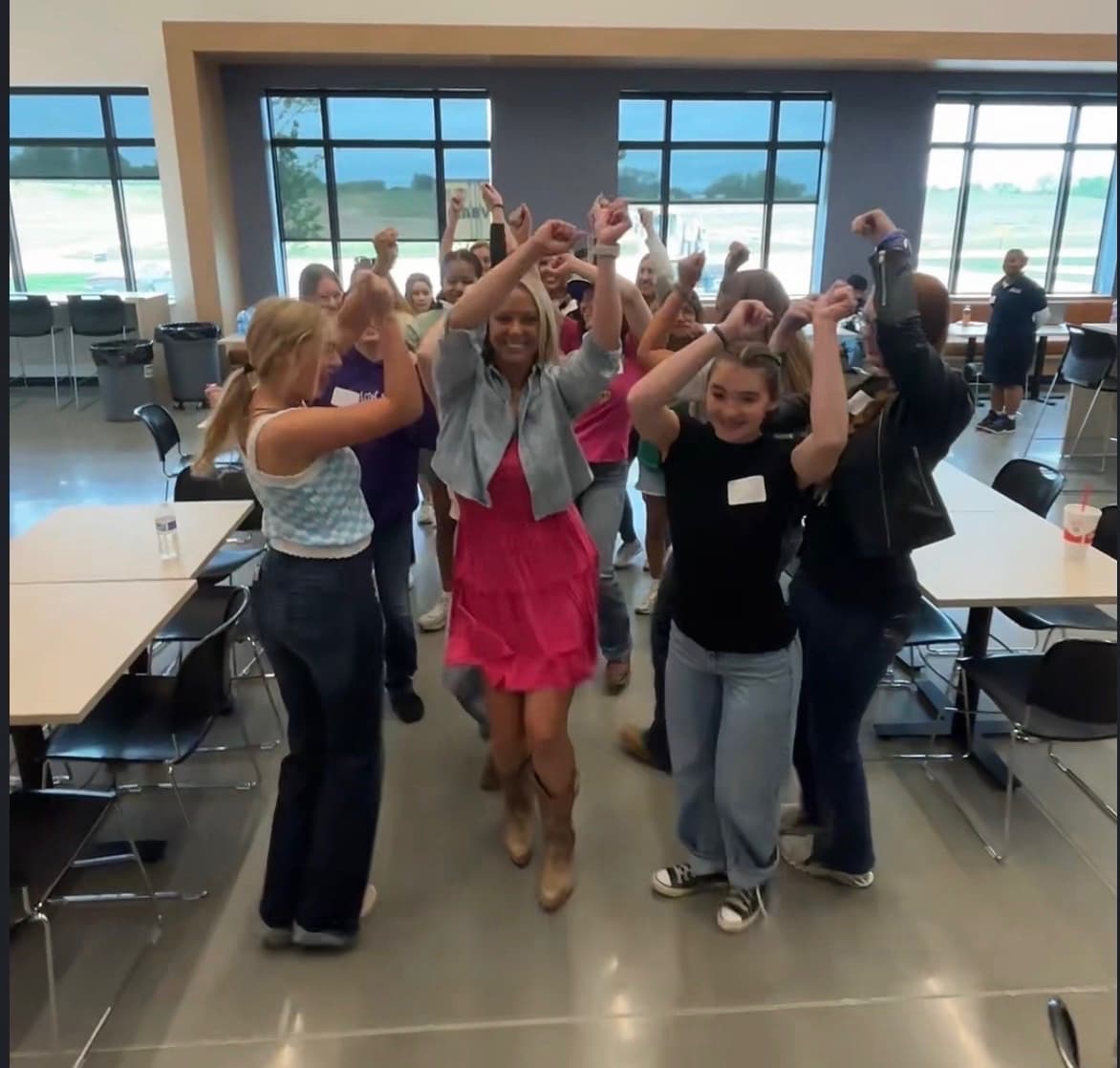 A group of women and students with their arms raised, cheering in a school commons