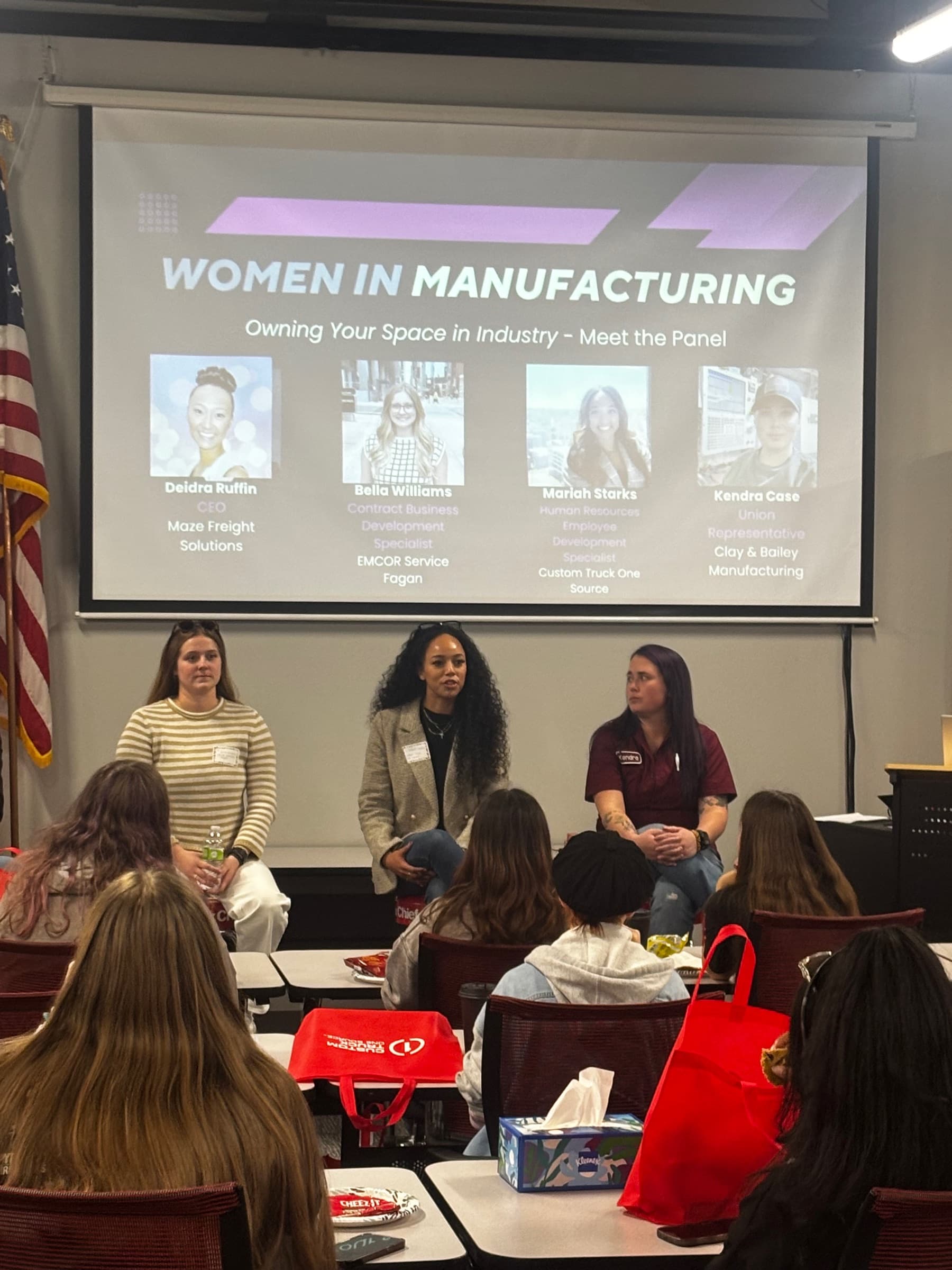 Three panelists seated in front of a Women in Manufacturing slide, an audience of women in the foreground