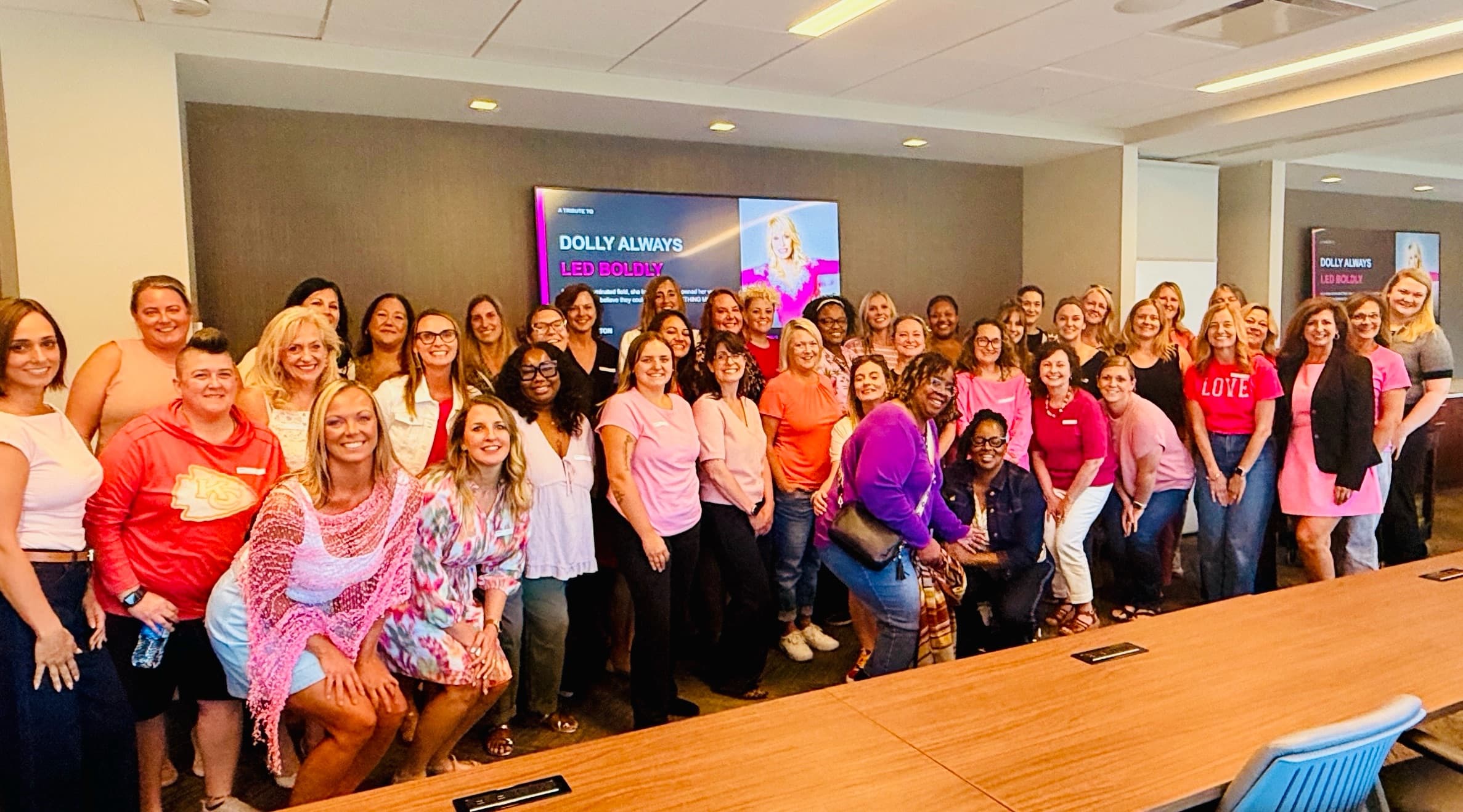 A crowd of women in pink filling a conference room for a She Leads event