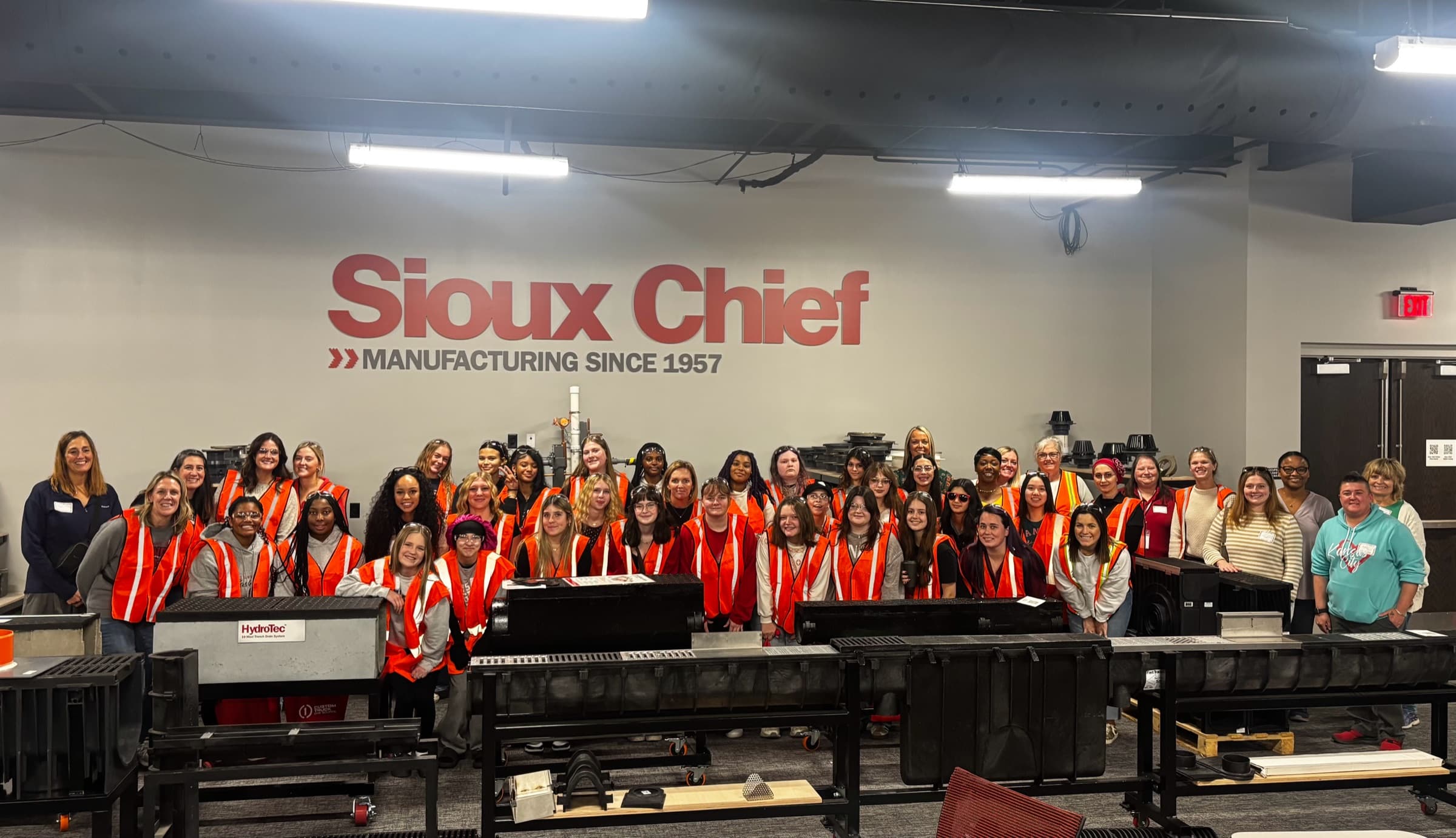 A large group of women in orange safety vests on the production floor at Sioux Chief