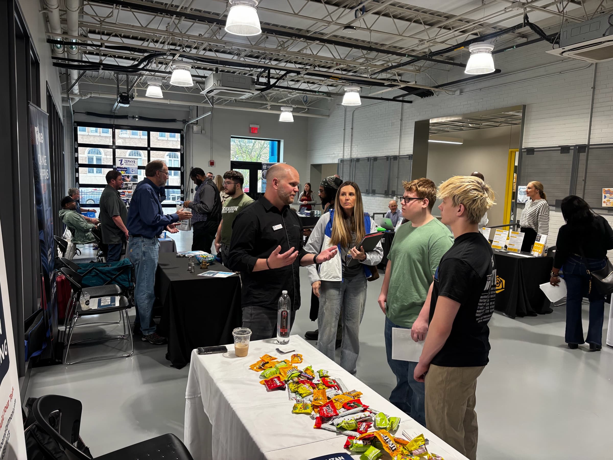An exhibitor in black talking with two students across a table at a career fair