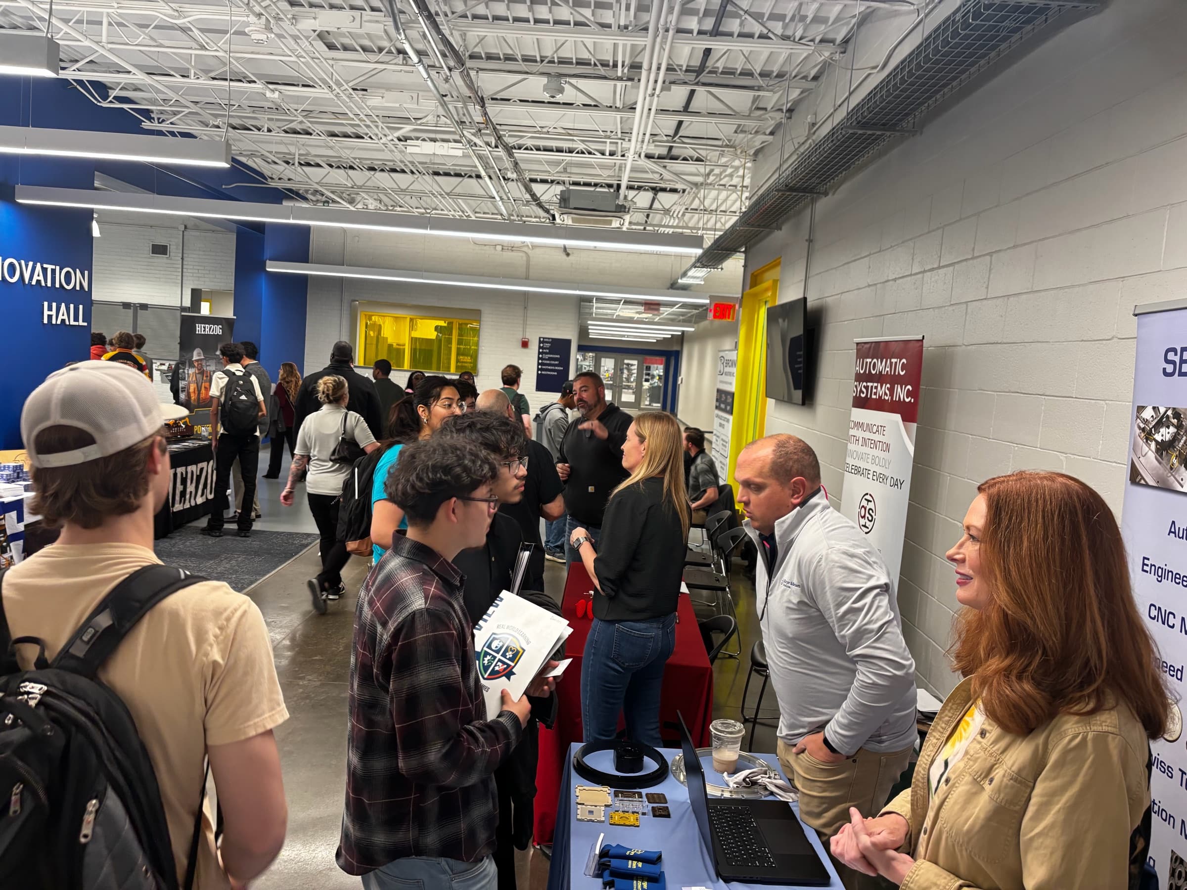 Students at a manufacturing booth in a school's Innovation Hall talking with two exhibitors